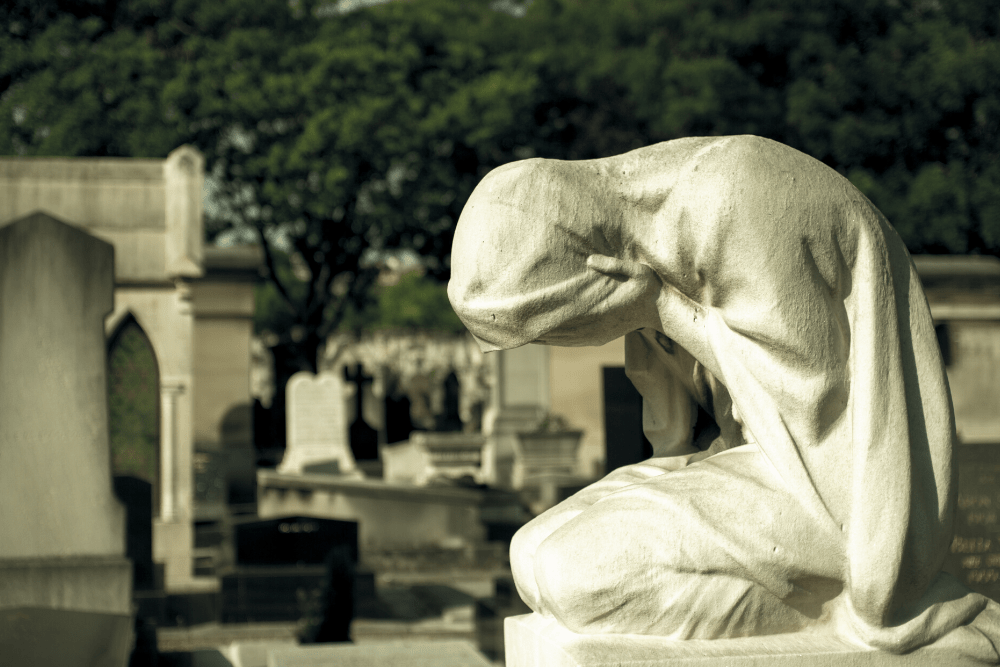 Statue of woman kneeling, crying with her face in her hands, showing sadness and loss.